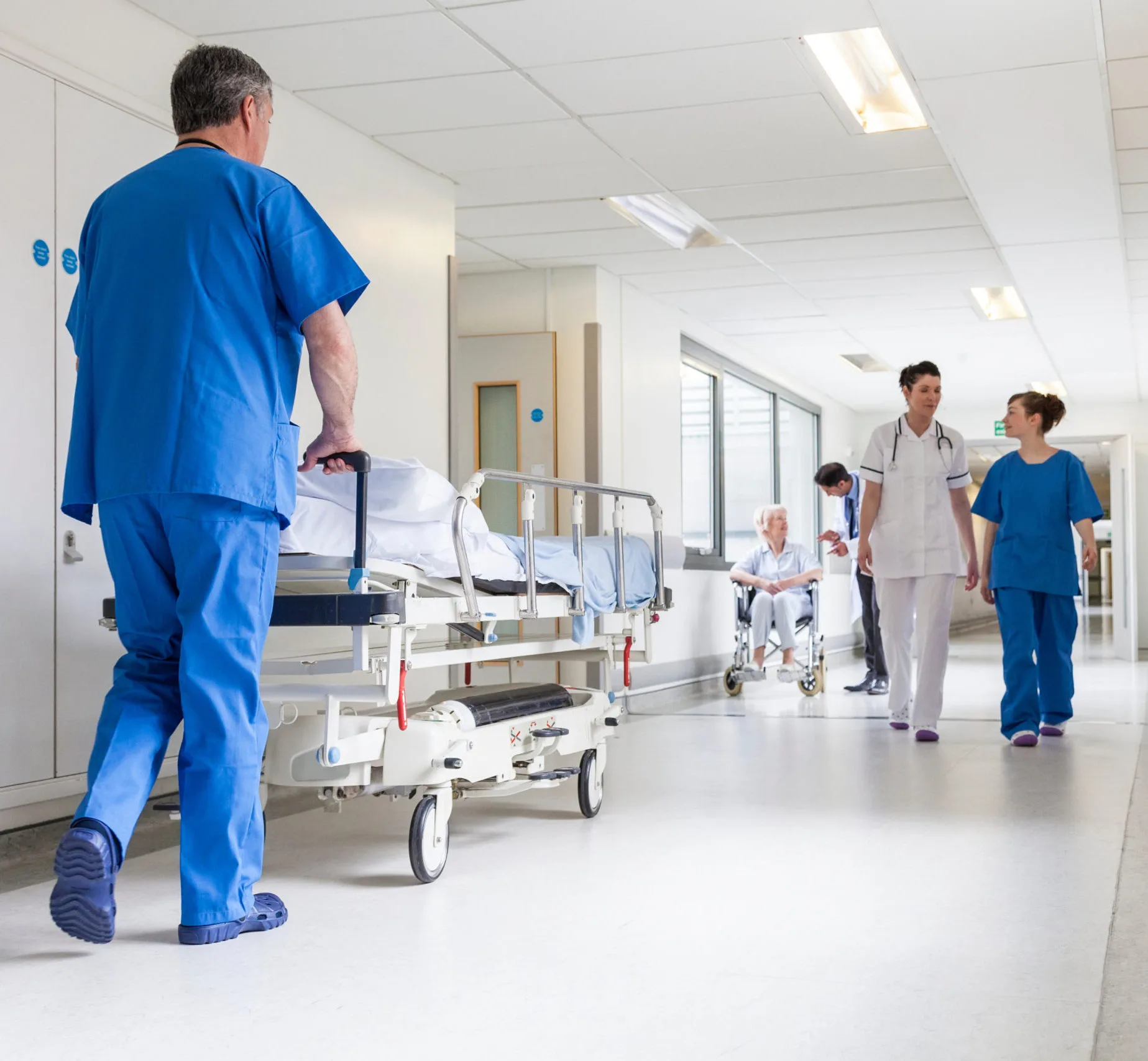 Hospital Orderly Pushing Patient Stretcher Through Busy Medical Corridor